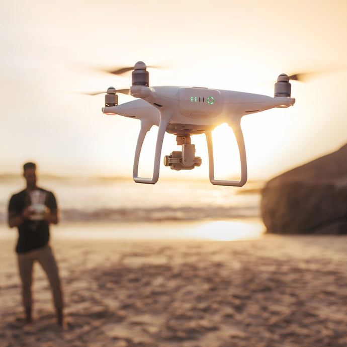 A white drone flying over a beach during sunset, operator with remote control.