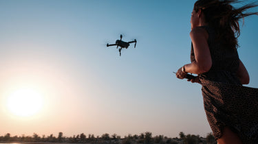 Person flying drone at sunset over a forest.