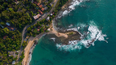 Lush tropical coastline with beaches, rocks, road, and houses.