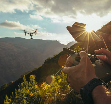 Person operating drone at sunset with mountainous backdrop. Mobile