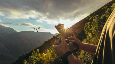 Person operating drone at sunset with mountainous backdrop.