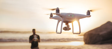 "A white drone flying over a beach during sunset, operator with remote control.